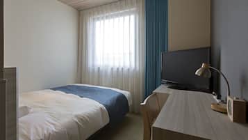 A hotel room with a bed, a desk with a television and lamp, and a window with curtains.