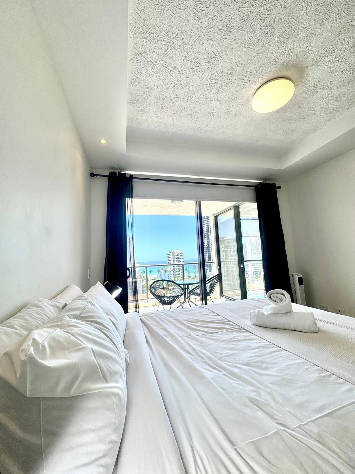 A hotel room with two beds, a balcony with a table and chairs, and a view of the sea.