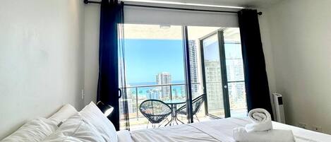 A hotel room with two beds, a balcony with a table and chairs, and a view of the sea.