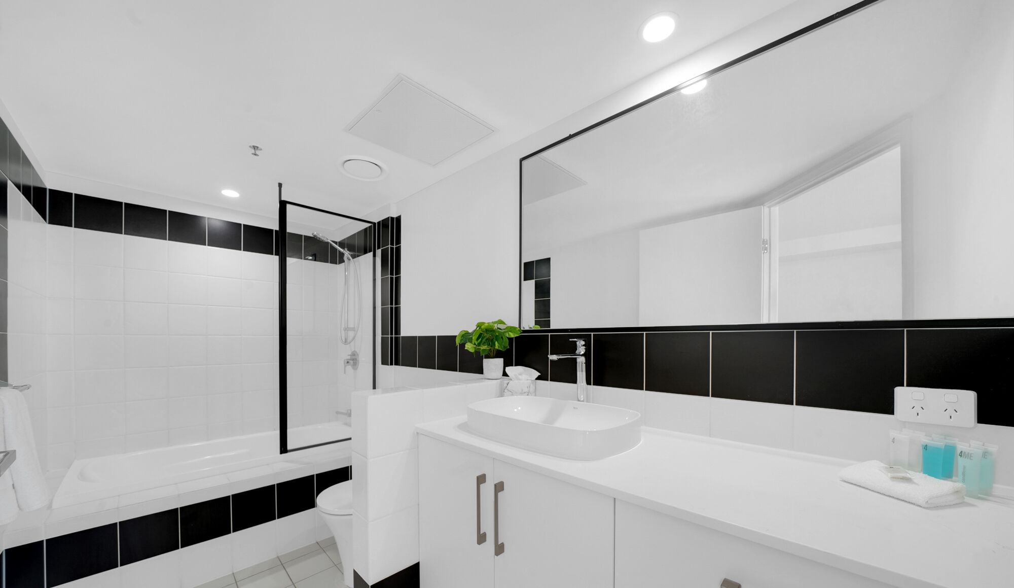 Une salle de bain moderne avec un lavabo blanc, des carreaux noirs et blancs, une douche en verre et un grand miroir.