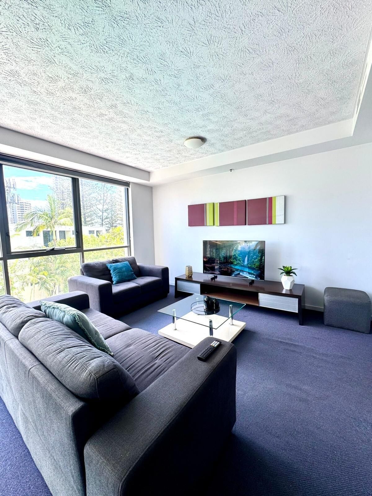 A modern living room with a large window, a sofa, a coffee table, a TV, and a decorative shelf.