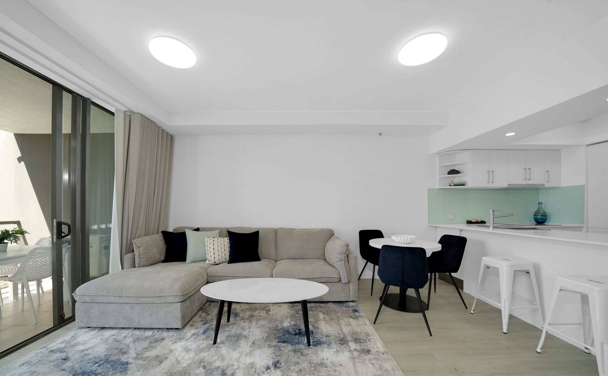 Una sala de estar moderna con un sofá modular, una mesa de centro redonda y un comedor con una mesa blanca y sillas negras.