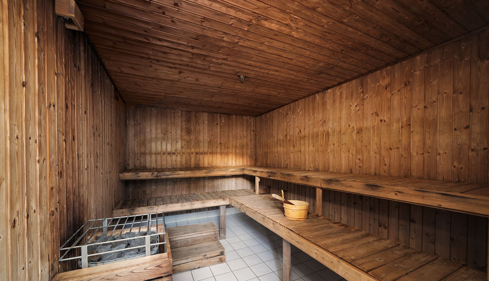 A wooden sauna with benches and a metal grate for heating.