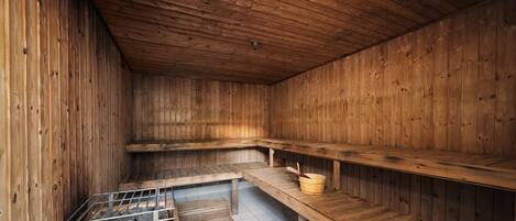 A wooden sauna with benches and a metal grate for heating.