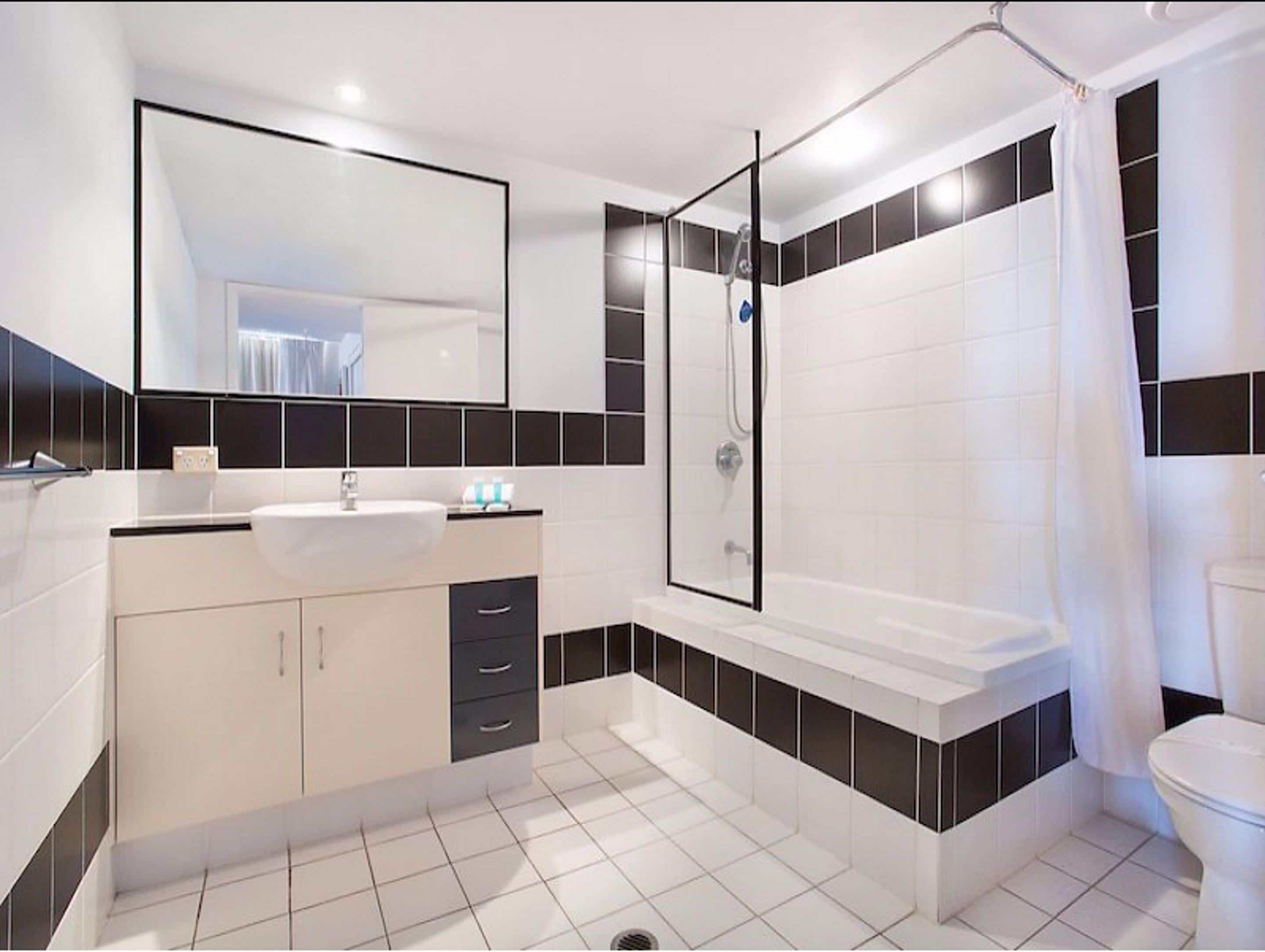 A modern bathroom with a white sink, black and white tiled walls, a glass shower enclosure, and a white toilet.