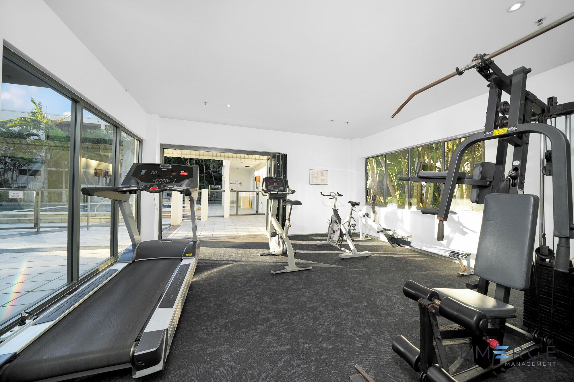 A modern gym with cardio equipment, weight machines, and a large window providing a view of the outdoors.