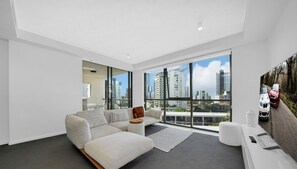 Una sala de estar moderna con un sofá grande, una mesa de centro y vistas a un paisaje urbano a través de amplios ventanales.
