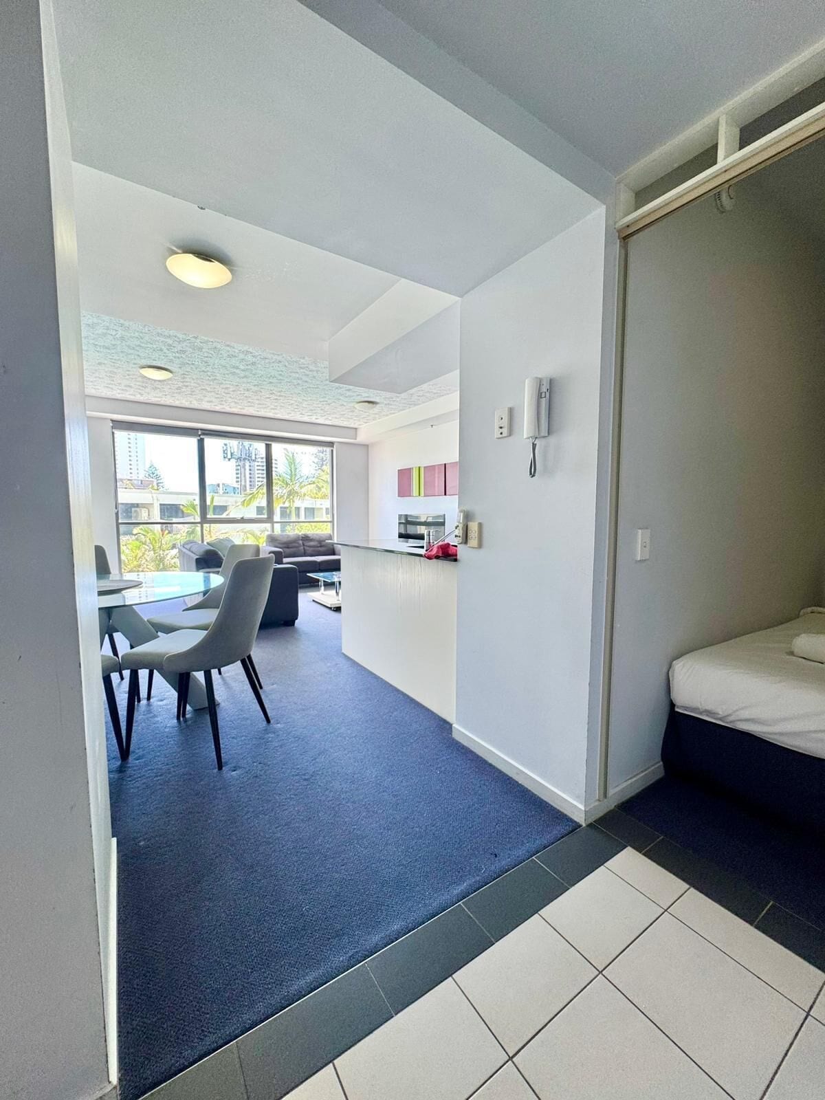 A modern hotel room with a bed, a small kitchenette, a dining area with a table and chairs, and a view of the outside.