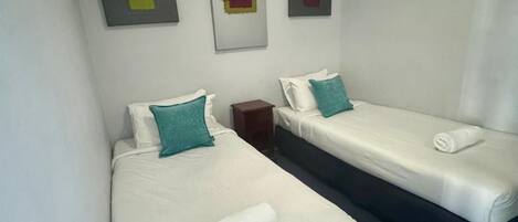 A hotel room with two single beds, a nightstand, and three abstract wall art pieces.