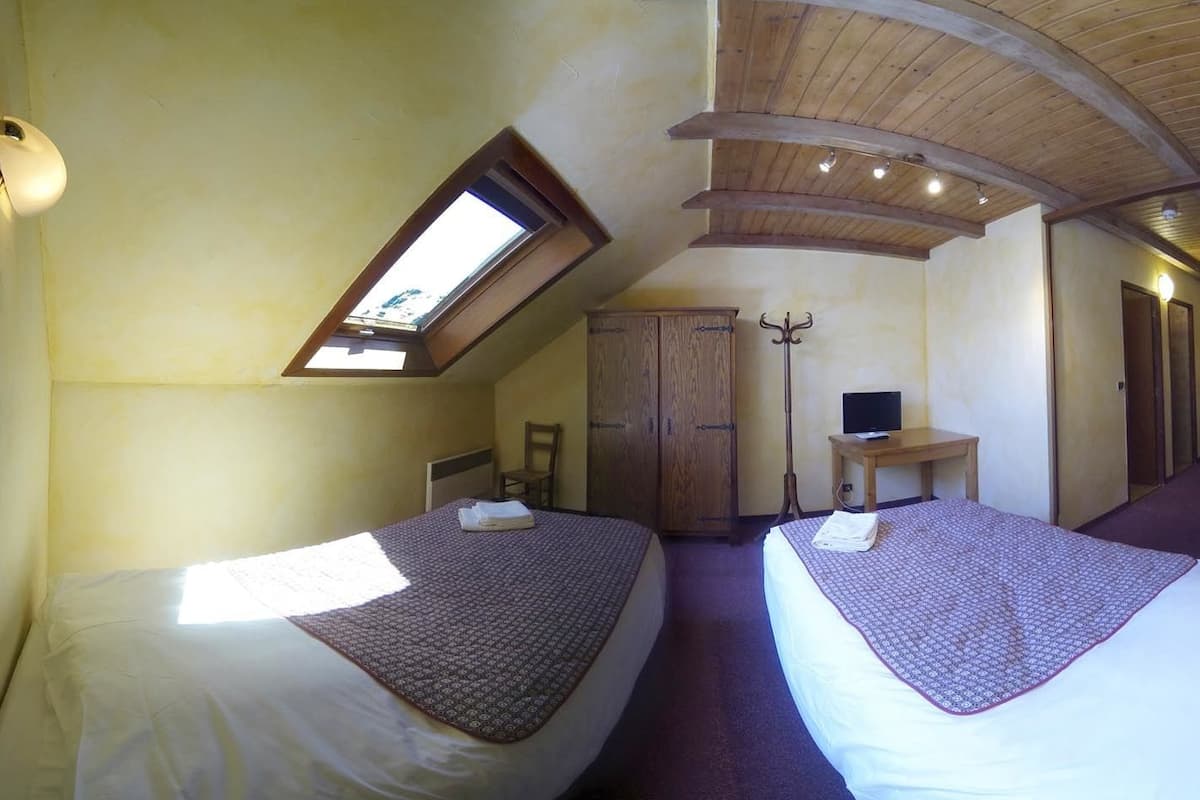 Een kamer met twee bedden, een houten garderobe, een bureau met stoel en een klein raam.