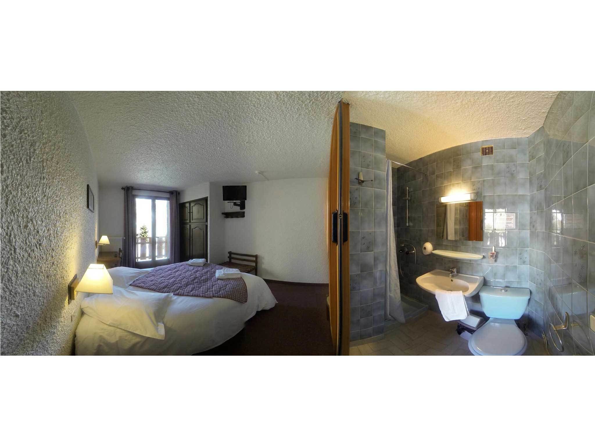 A hotel room with a bed, a bedside lamp, a shower area, and a bathroom with a sink and toilet.