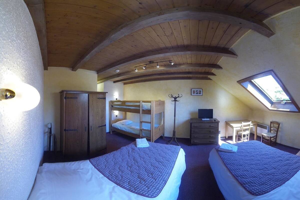 Een kamer met twee stapelbedden, een houten garderobe, een bureau met stoel, een dressoir en een kleine tafel met stoel. Boven het bureau is een dakraam.