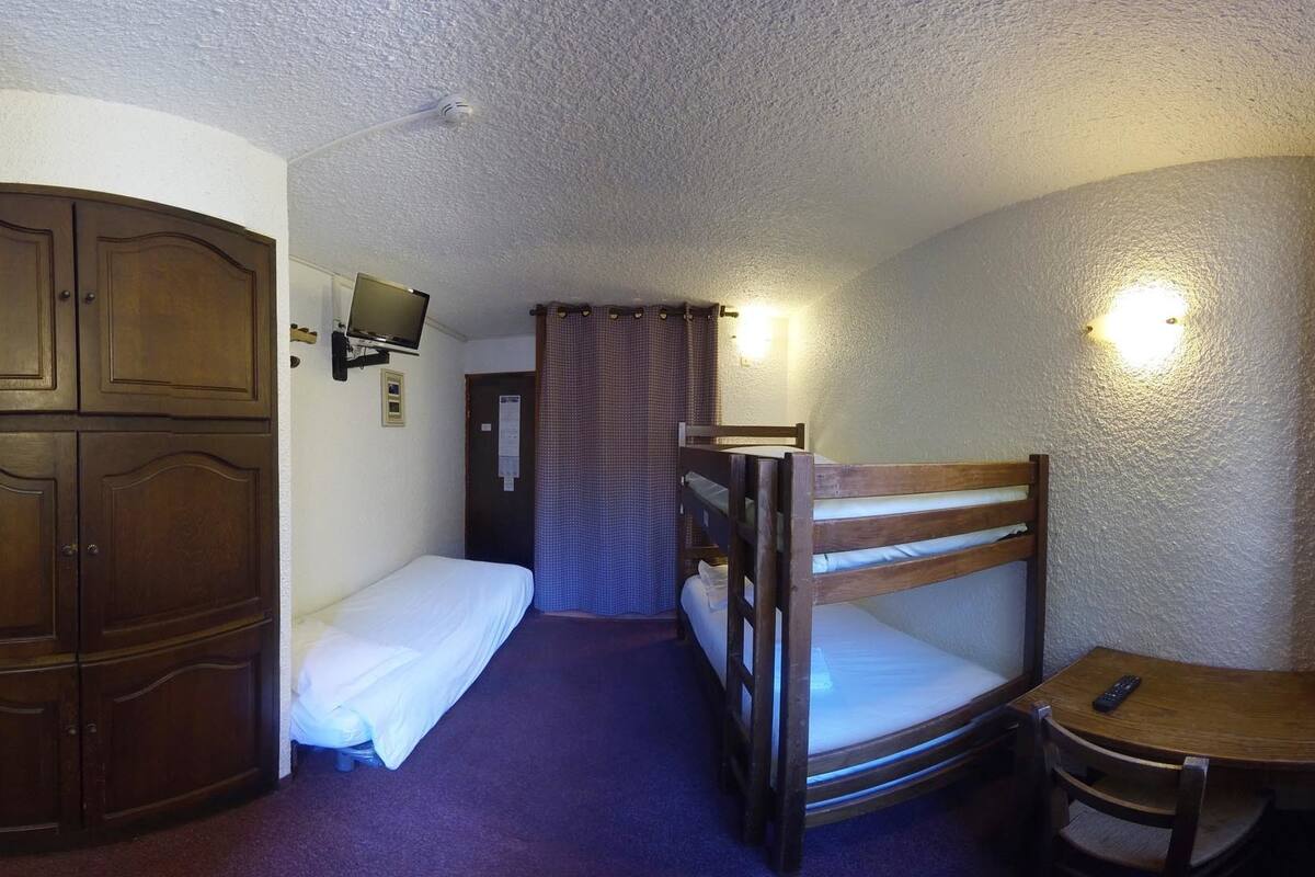 Een compacte hotelkamer met twee stapelbedden, een houten garderobe, een klein tafeltje met een stoel en een aan de muur bevestigde televisie.