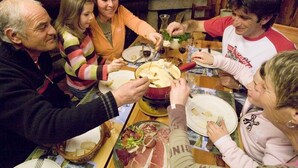 Un grupo de personas reunido alrededor de una mesa con comida y bebidas, en una habitación con muebles de madera y chimenea.