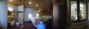 Cozy retreat with a sloped ceiling, featuring a bed, bedside table, and window with a view of the surrounding trees.