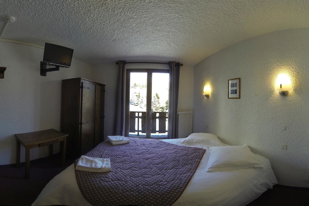 Een slaapkamer met een bed, een bureau, een kledingkast, een televisie en een raam met gordijnen.