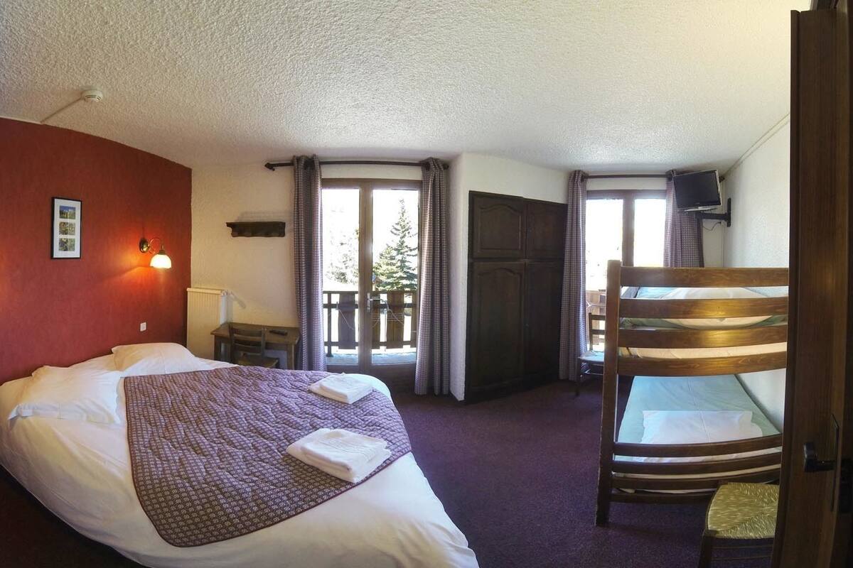 Een hotelkamer met een bed, bureau, stoel en een balkon met gordijnen.