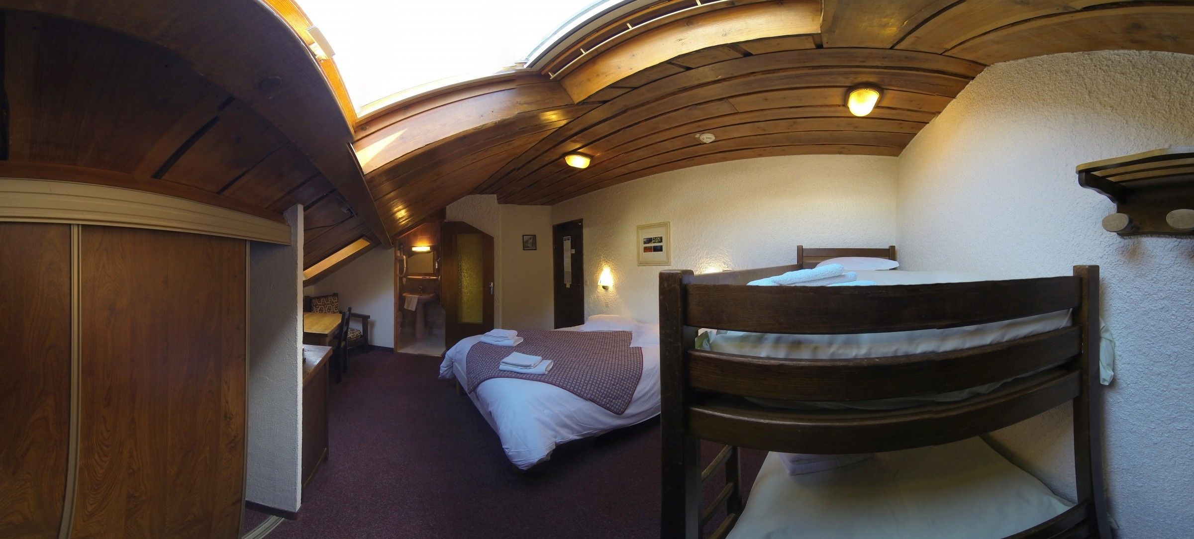 A cozy room with a wooden ceiling, a bed with a white and brown blanket, and a chair.
