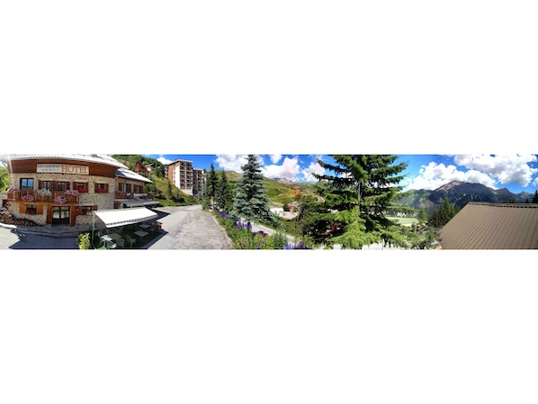 Traditional hotel with a stone facade and wooden balconies, set amidst scenic mountains.