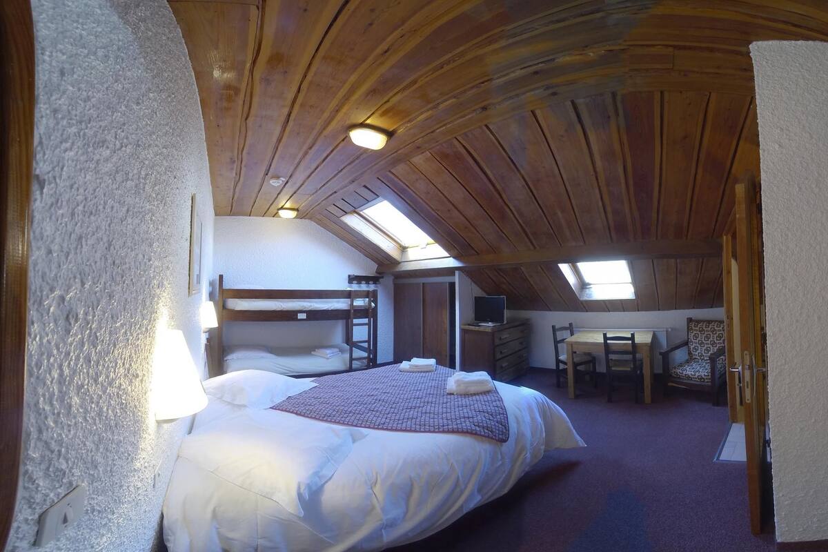 Een gezellige slaapkamer met een groot bed, een bureau en een stoel, met houten plafonds en dakramen.