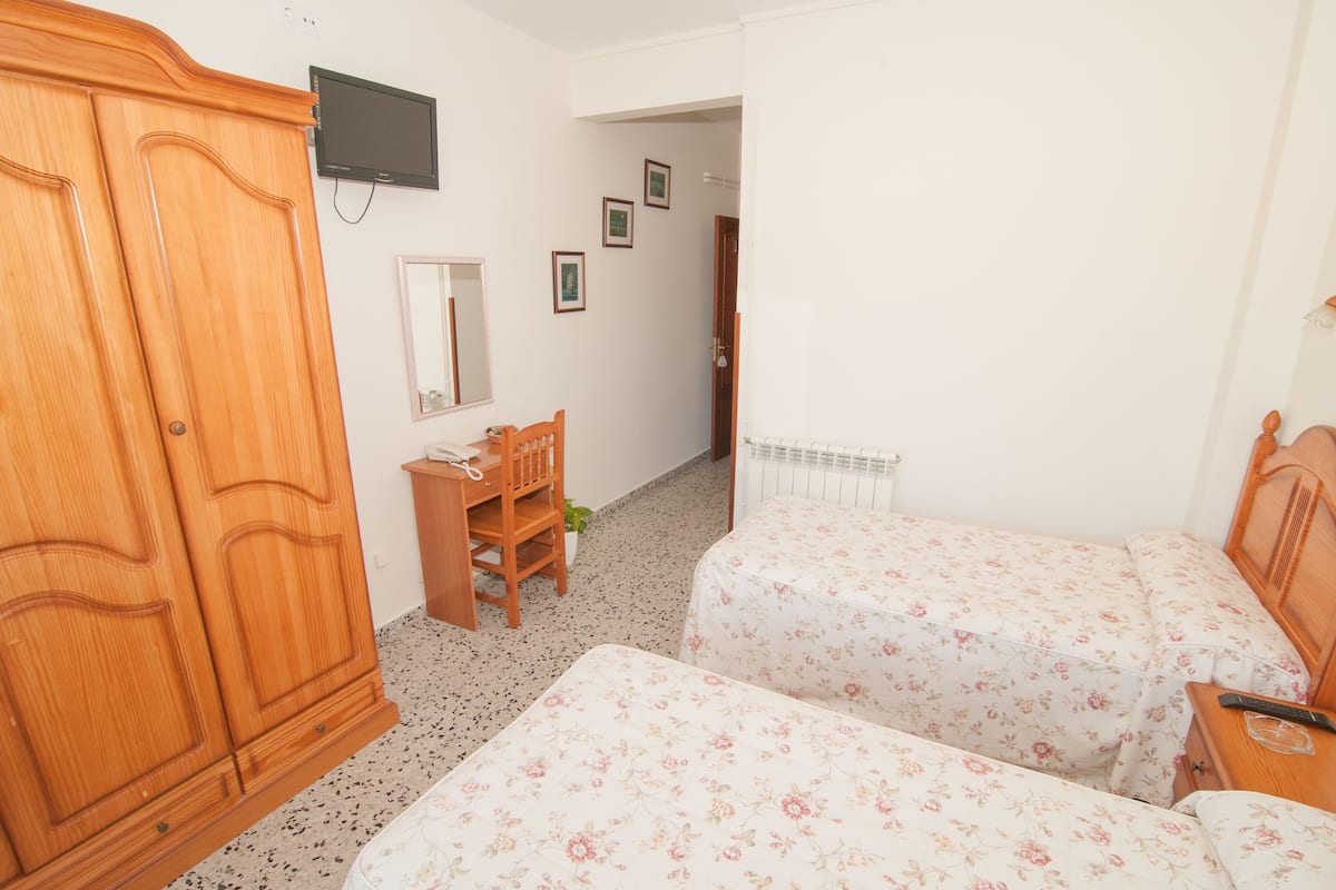 A bedroom with two beds, a wooden wardrobe, a desk, a chair, a television, and a radiator.