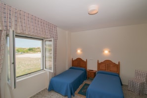 A bedroom with two single beds, a window with curtains, a small bedside table, and a chair. - Hotel Costa de Ajo (Bareyo)