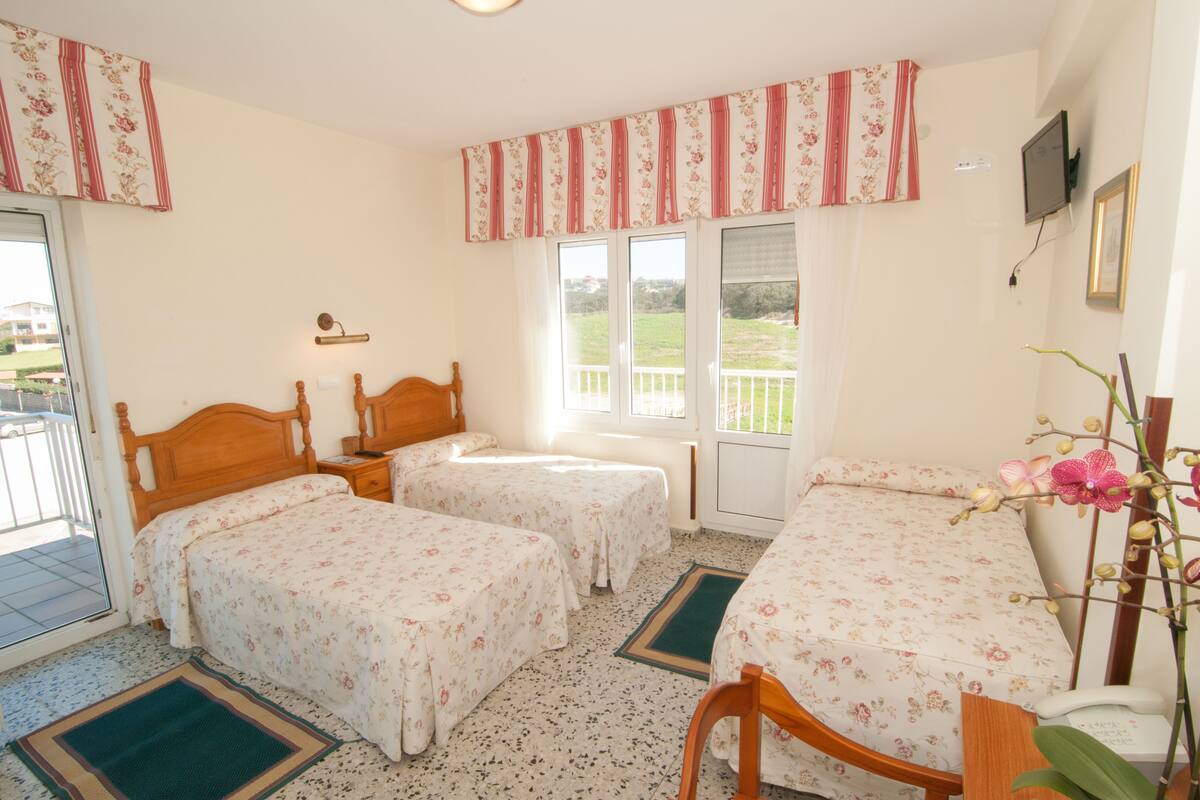 A room with two single beds, a wooden chair, a desk with a telephone, and a TV on the wall.