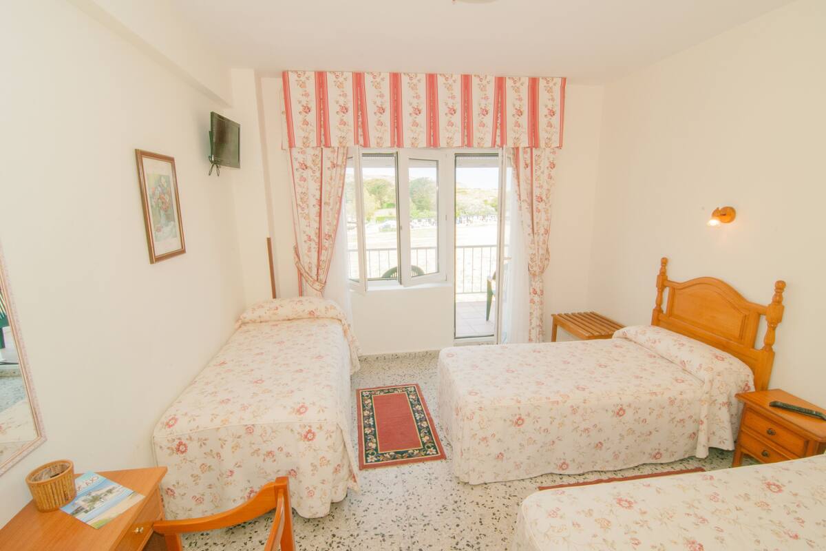 A room with two single beds, a wooden nightstand, a small table with a basket, and a framed picture on the wall.
