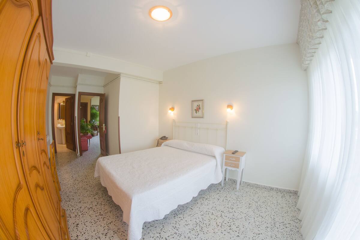 A bedroom with a bed, bedside table, and a nightstand. There is a door leading to another room.