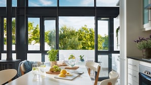 A modern kitchen with a dining area, large windows, and a view of greenery. - Eikehoff Apartment  (Stellenbosch)