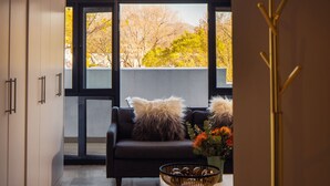 A modern living room with a dark sofa, two fluffy pillows, a coffee table with a woven basket, and a vase with flowers. - Eikehoff Apartment  (Stellenbosch)