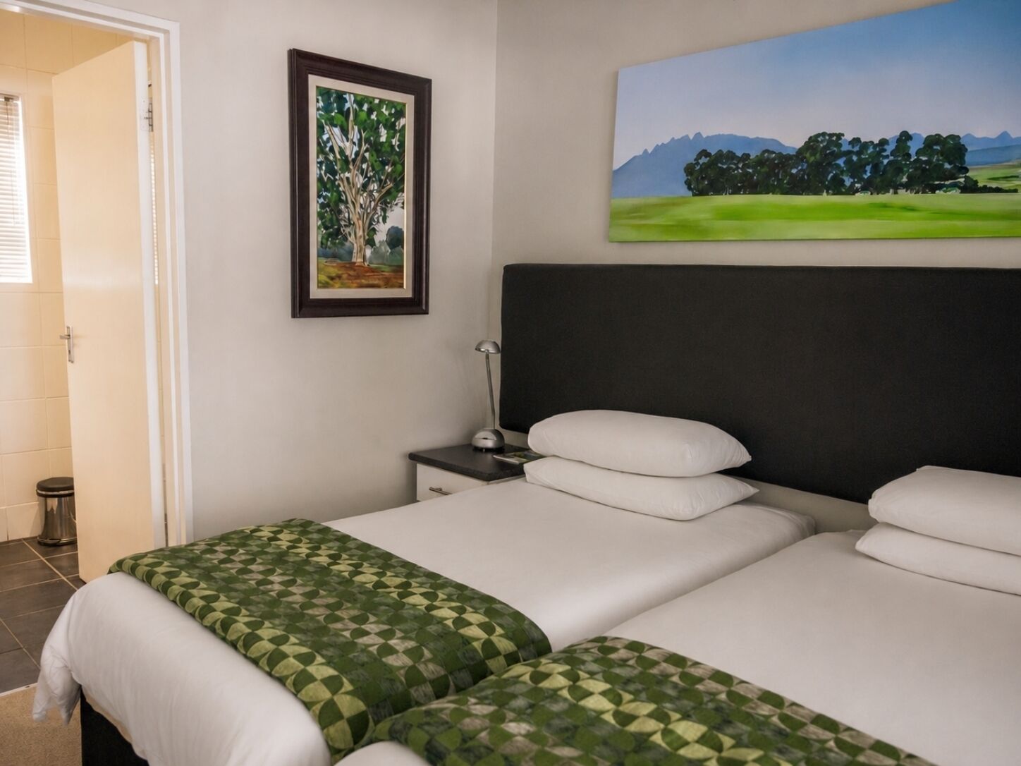 Una habitación de hotel con una cama, una mesita de noche, una lámpara y un cuadro en la pared.
