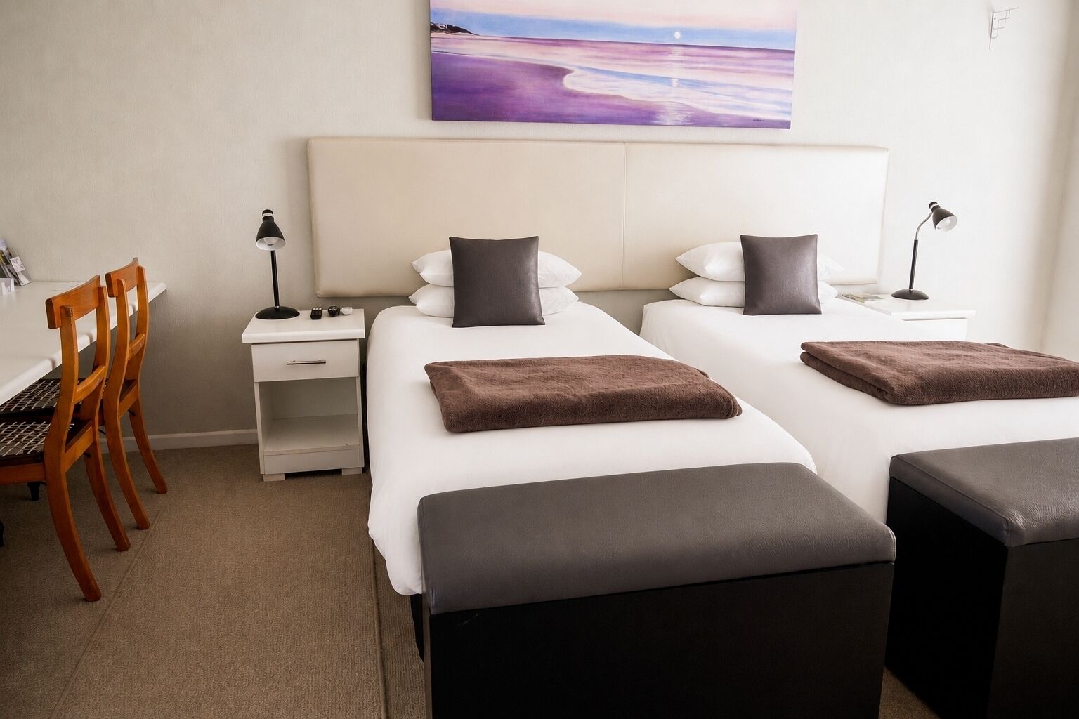 Quarto de hotel com duas camas, uma escrivaninha e uma cadeira.