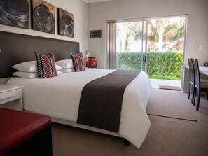 Habitación de hotel con cama, mesita de noche y vistas a la vegetación a través de una puerta corredera.