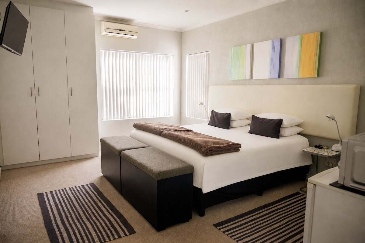 Een moderne slaapkamer met een bed, nachtkastjes, een bankje en kunst aan de muur.