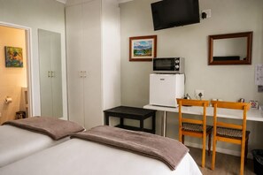 A hotel room with a bed, a desk with a microwave, a chair, and a TV on the wall. - Monte Vidéo Guest House (Wellington)