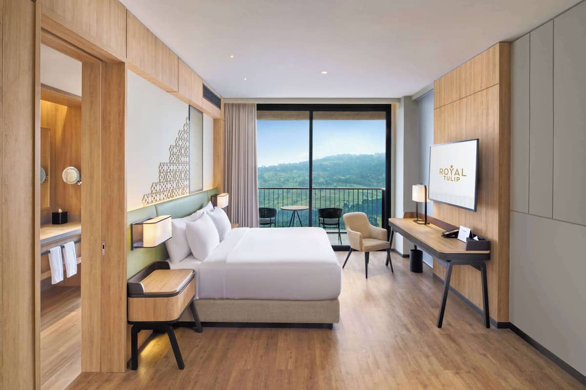 Ein Hotelzimmer mit einem großen Bett, einem Schreibtisch, einem Stuhl und einem Balkon mit Blick.