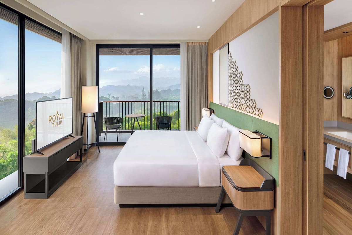 Ein Hotelzimmer mit einem großen Bett, einem Fernseher, einem Balkon mit Blick und einem Holzkasten.