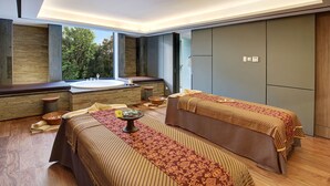 Une salle de spa équipée de deux lits, d’une grande baignoire et offrant une vue sur les arbres.