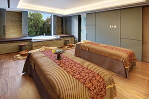 Ein Spa-Zimmer mit zwei Betten, einer großen Badewanne und Blick auf Bäume.