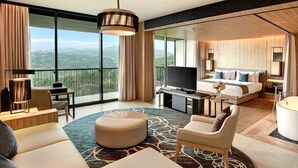 Ein modernes Hotelzimmer mit einem großen Bett, einer Sitzecke mit Sofa und Hocker, einem Fernseher und einem Badezimmer mit Badewanne.