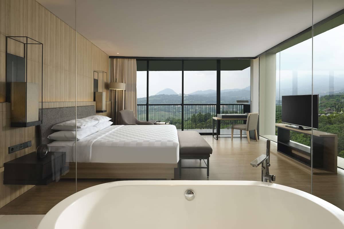 Ein modernes Hotelzimmer mit einem großen Bett, einer Sitzecke, einem Fernseher und einem Balkon mit Bergblick.