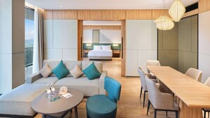 Ein modernes Hotelzimmer mit Sofa, Hocker, Esstisch und einem Bett im Hintergrund.