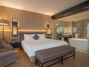Ein modernes Hotelzimmer mit einem großen Bett, Nachttischen, einer Bank, einer Couch, einem Badezimmer mit Duschkabine aus Glas und einem großen Spiegel.