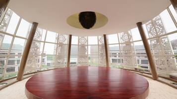 A circular wooden table in a room with large windows and decorative lattice panels.
