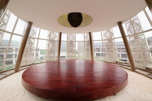 A circular wooden table in a room with large windows and decorative lattice panels. - Golden Tulip Jineng Resort Bali (Kuta)