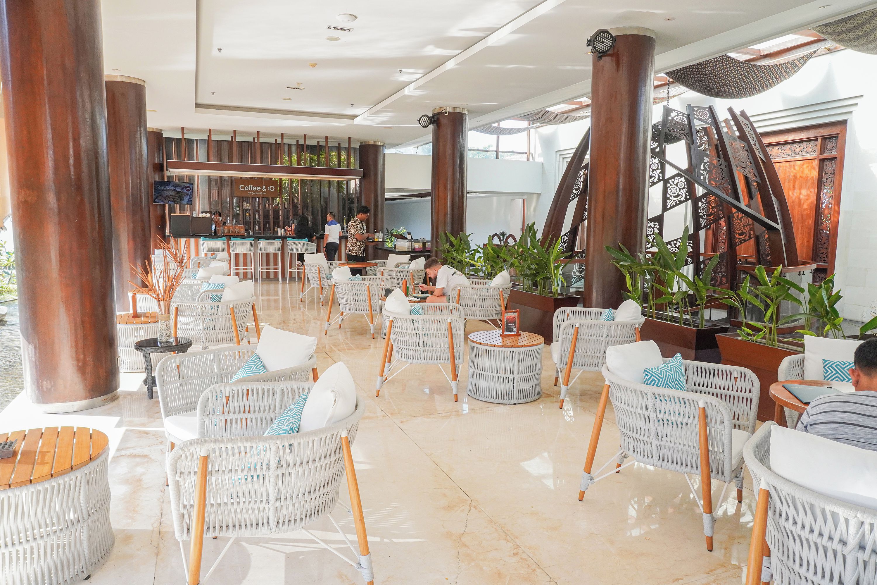 A spacious indoor area with white wicker furniture, a bar area, and large columns.