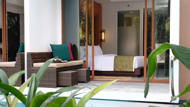 Ein Hotelzimmer mit einem Bett, einer Sitzecke mit Kissen und Blick auf einen Swimmingpool.