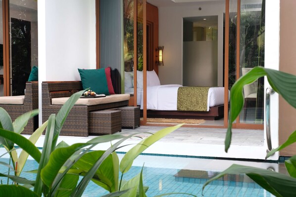 A hotel room with a bed, a seating area with cushions, and a view of a swimming pool. - Golden Tulip Jineng Resort Bali (Kuta)