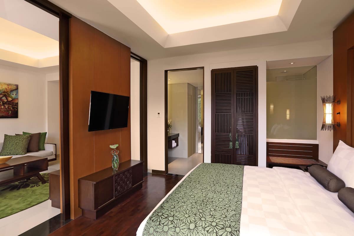 Ein modernes Hotelzimmer mit einem großen Bett, einem Flachbildfernseher, einer Holzkonsole und einer zudeckenden Bettwäsche mit grünem Muster.